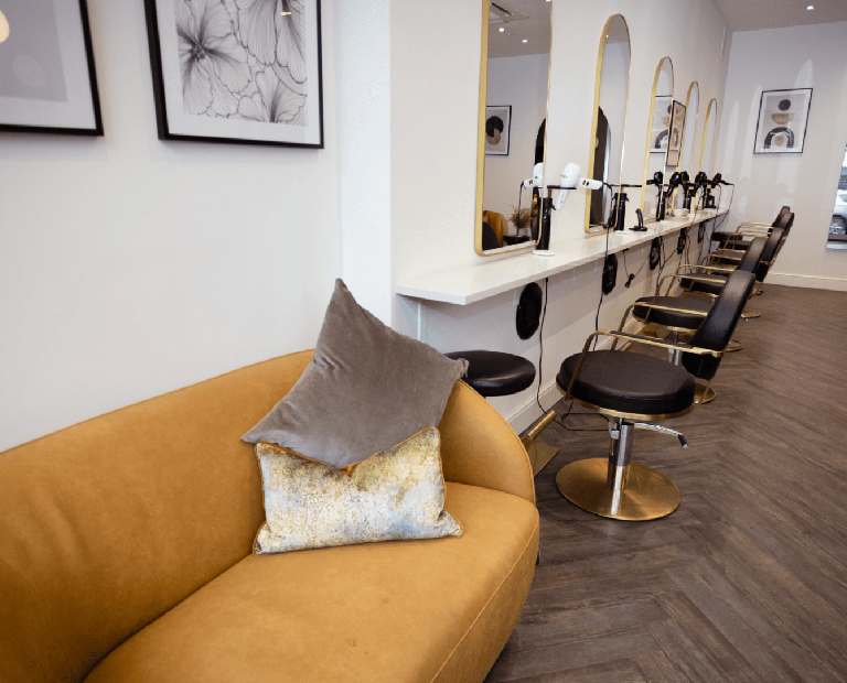 Interior of The Cutting Company Salon, gold couches and black seats infront of mirrows.